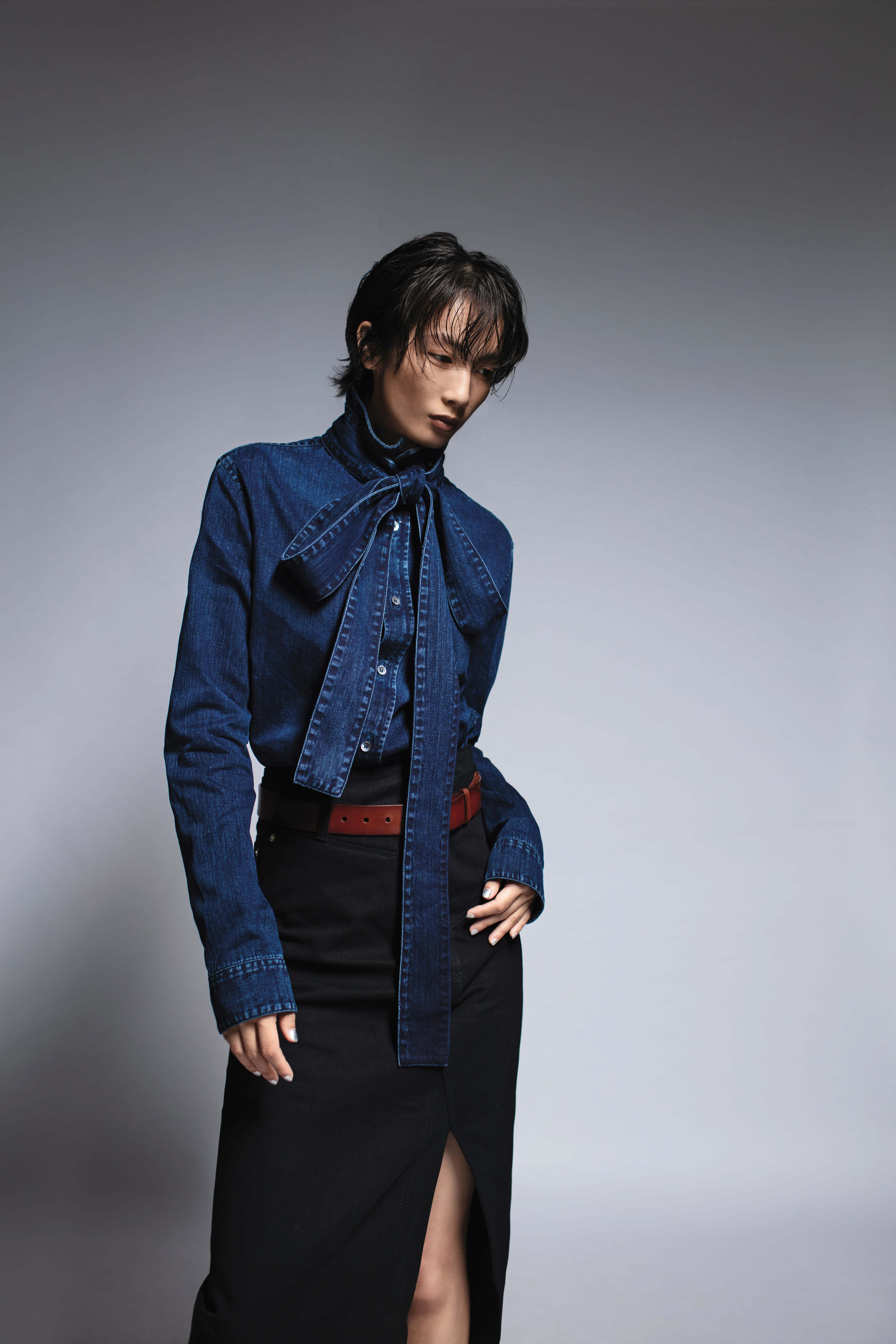 丹寧蝴蝶結襯衫 NT$39,000 by Loewe／黑色直筒牛仔裙 價格店洽 by Loewe／棕色腰帶 價格店洽 by Saint Laurent 