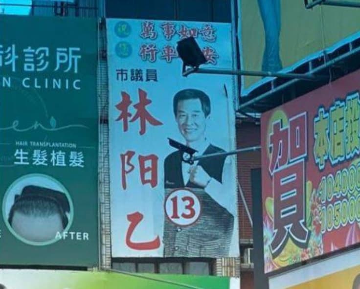 前台南市議員林阳乙在2020年的廣告看板前,就因投射燈的角度,讓不少人誤以為他拿著「手槍」。(翻攝自新·路上觀察學院)