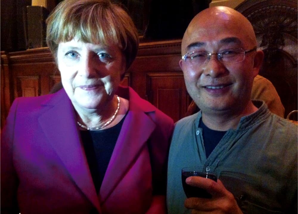 2014年,廖亦武(右)在柏林圍牆倒塌25週年音樂會和德國總理梅克爾(左)聊天,他滿臉通紅,已有醉意。(廖亦武提供)