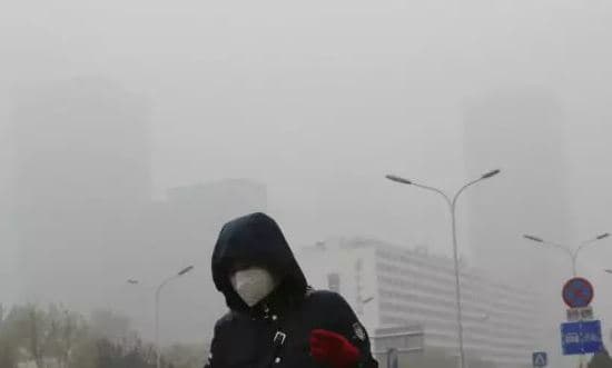 一個戴著口罩的行人走在煙霧繚繞的北京街頭（Andy Wong/AP）