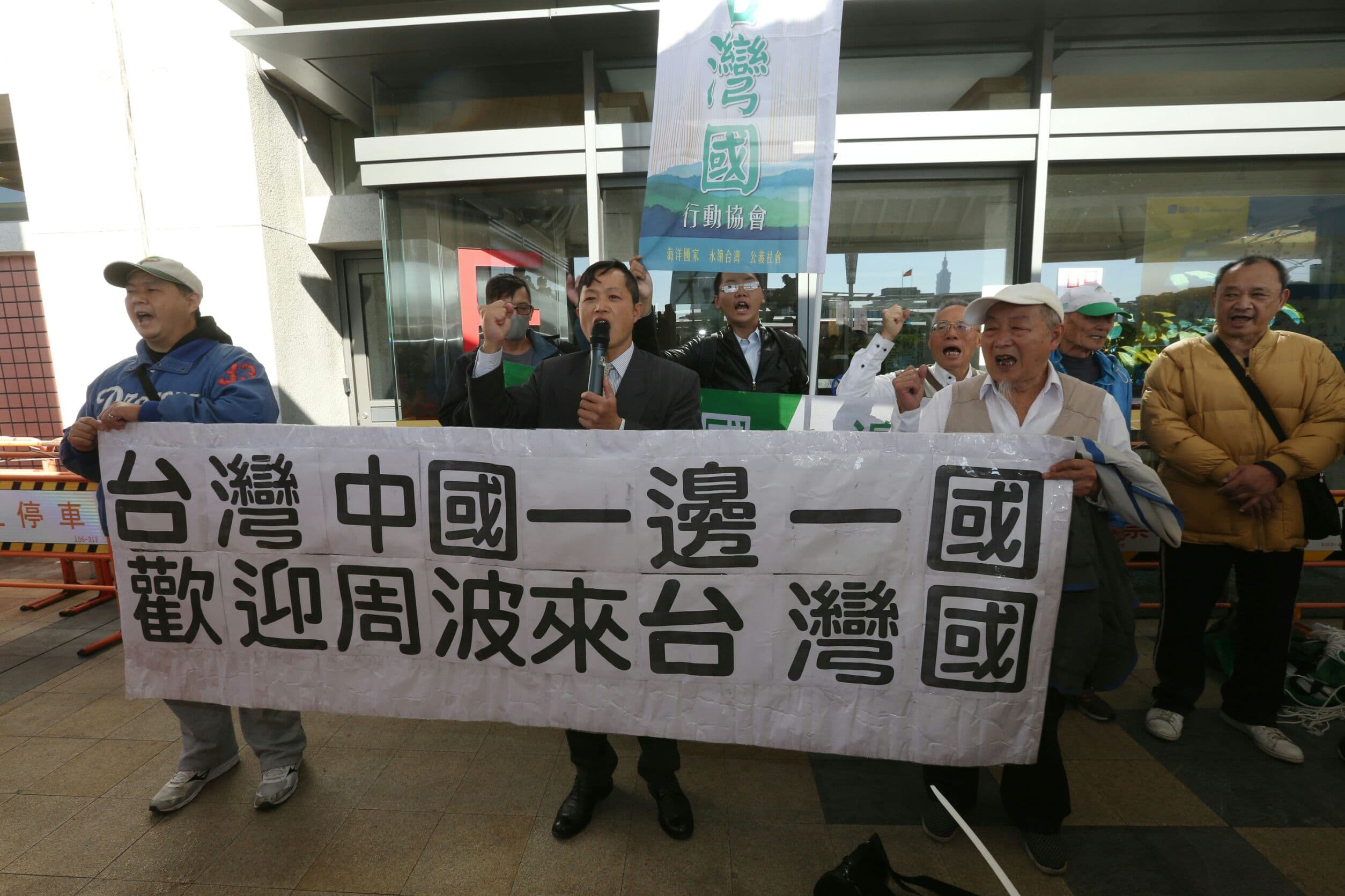 周波抵台後,出機場前碰到台灣國成員大喊高舉布條大喊「台灣中國一邊一國」。