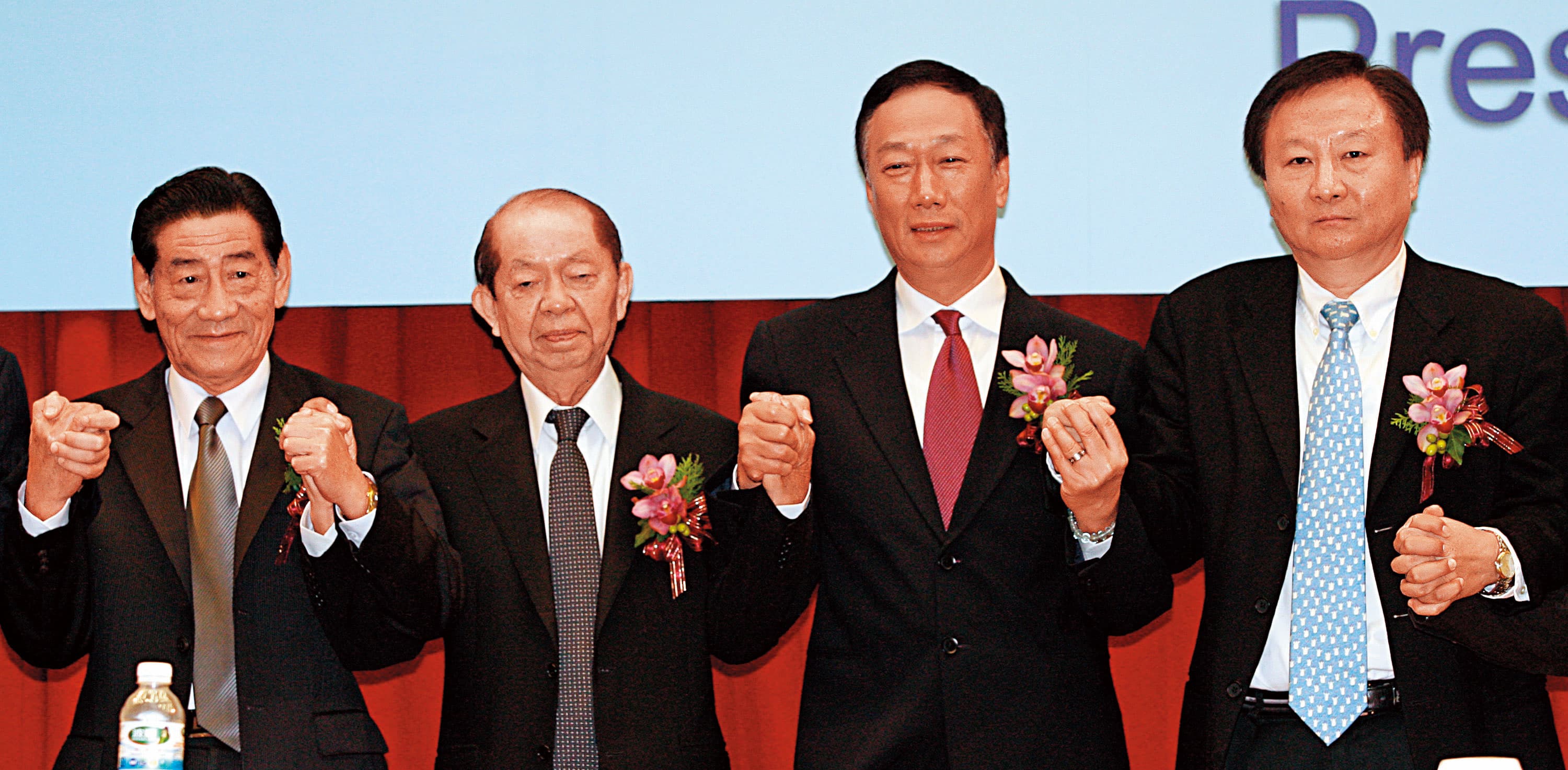 2009年鴻海董事長郭台銘(右2)手牽奇美集團創辦人許文龍(左2),宣布奇美電與群創光電合併。(中央社)