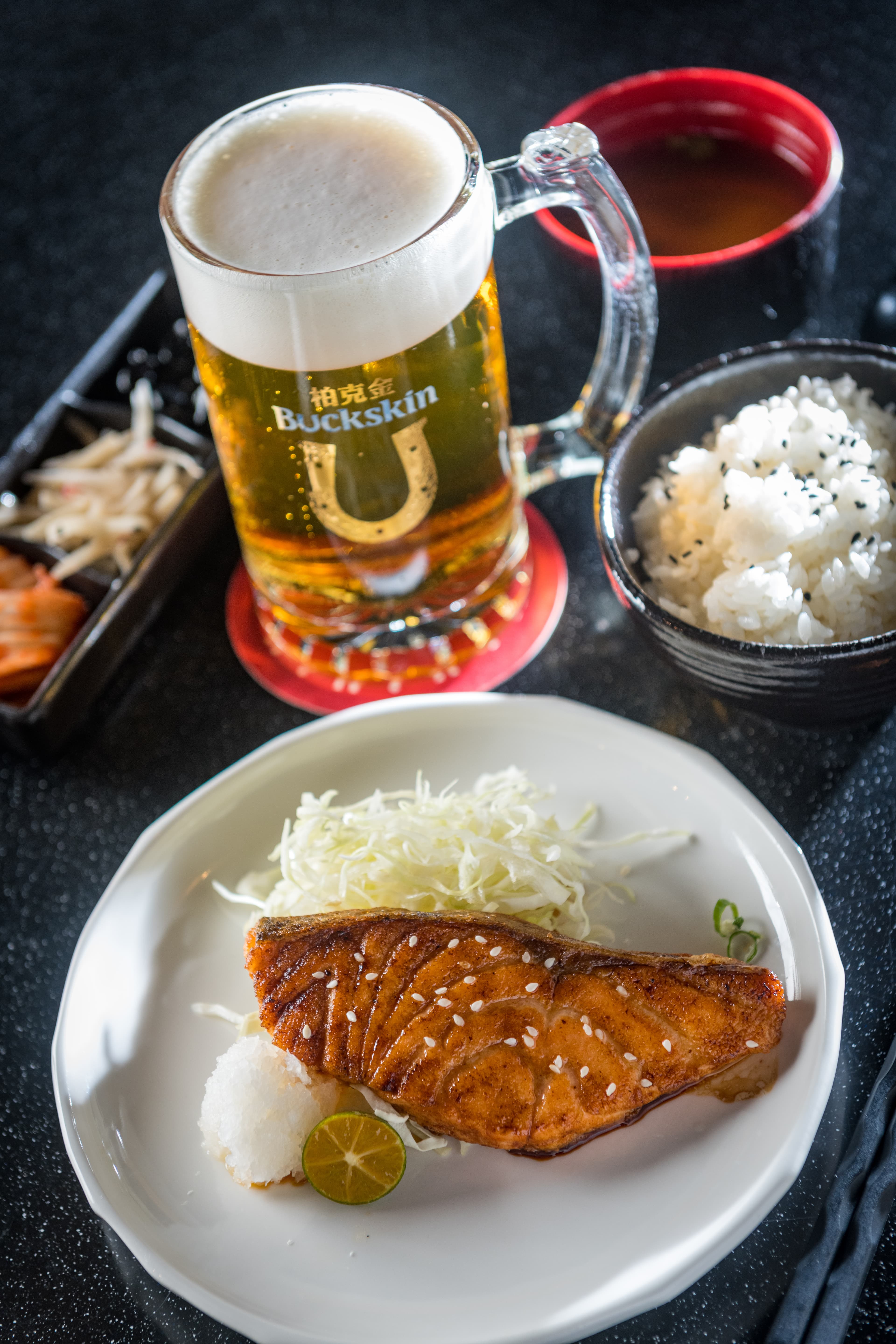 輕盈麥芽風味的「黃金拉格啤酒」（後，260元／500ml）可解「烤鮭魚定食」的豐厚油脂感（前，280元／份，商業午餐）