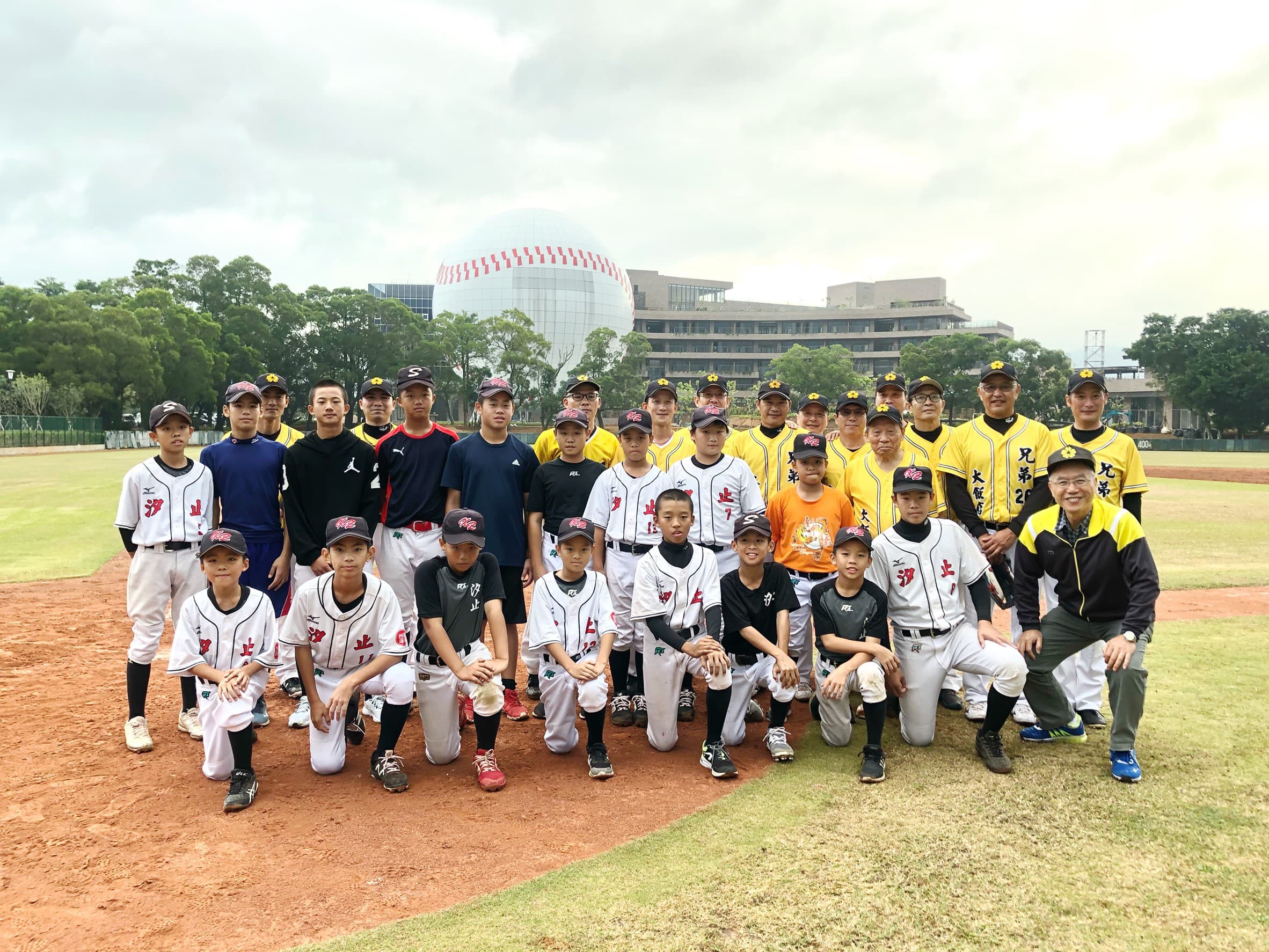 賽後,洪騰勝董事長率兄弟飯店與汐止國小棒球隊與賽球員合照,畫面後方高達32公尺的球體建築,就是今年11月底即將開幕的棒球名人堂。