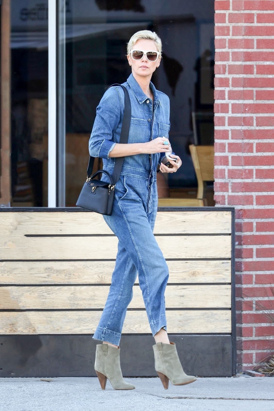 莎莉賽隆好帥氣啊!丹寧連身jumpsuit腳踩高跟短靴,搭配黑色Capucines Mini。(Louis Vuitton提供)