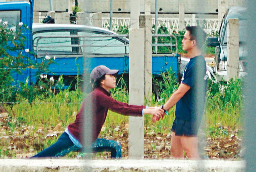 4月25日12:49,跑步前,吳彭弘(右)跟簡芳貞(左)先在路邊拉筋,2人拉著雙手,簡蹲下伸展下肢,整體看起來滑稽。