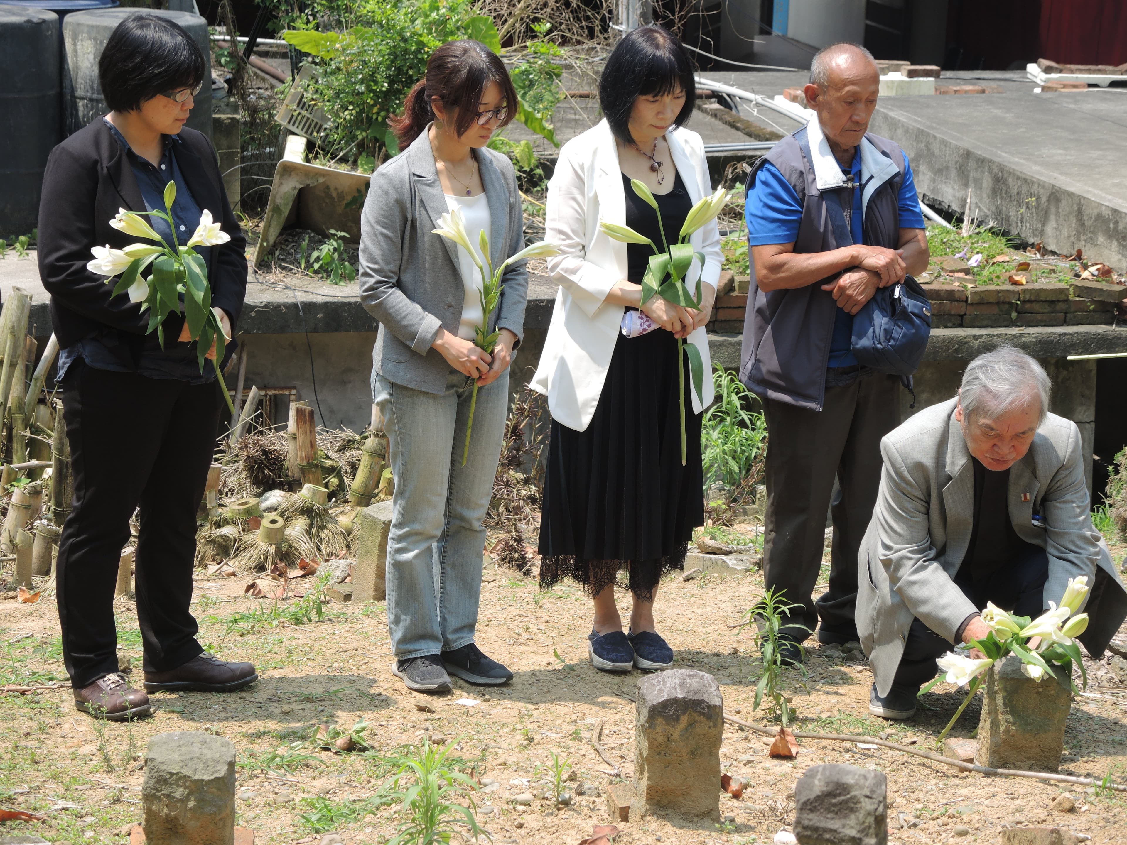 促轉會主委楊翠(左3)、彭仁郁委員(左2)、副主委葉虹靈(左1)、牧師伍錐(右1),陪同布農族原住民伍金山(右2)到六張犁政治受難者的亂葬崗,挖掘父親伍保忠的遺骨。(促轉會提供)