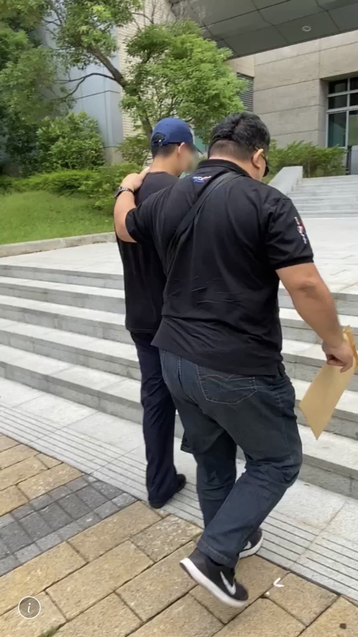 王姓網友(戴藍帽者)被警方帶回警局偵訊。(讀者提供)