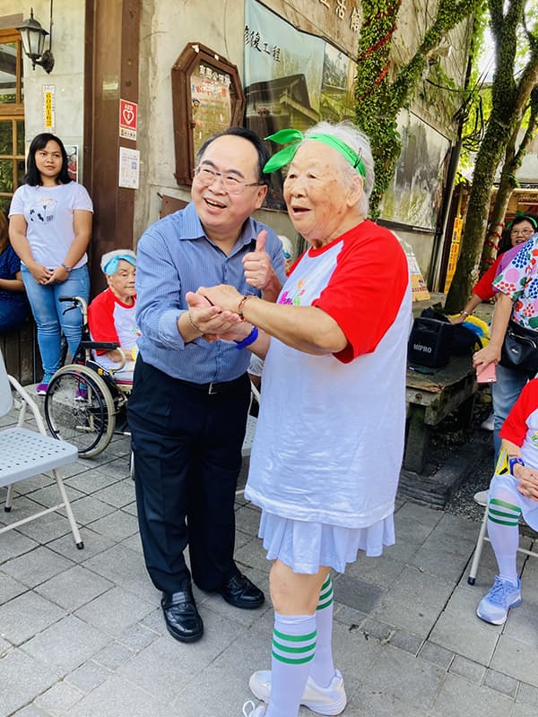 新北市社會局副局長林昭文(左)接受95歲奶奶親手編制手環祝福長壽健康。(一粒麥子基金會提供)