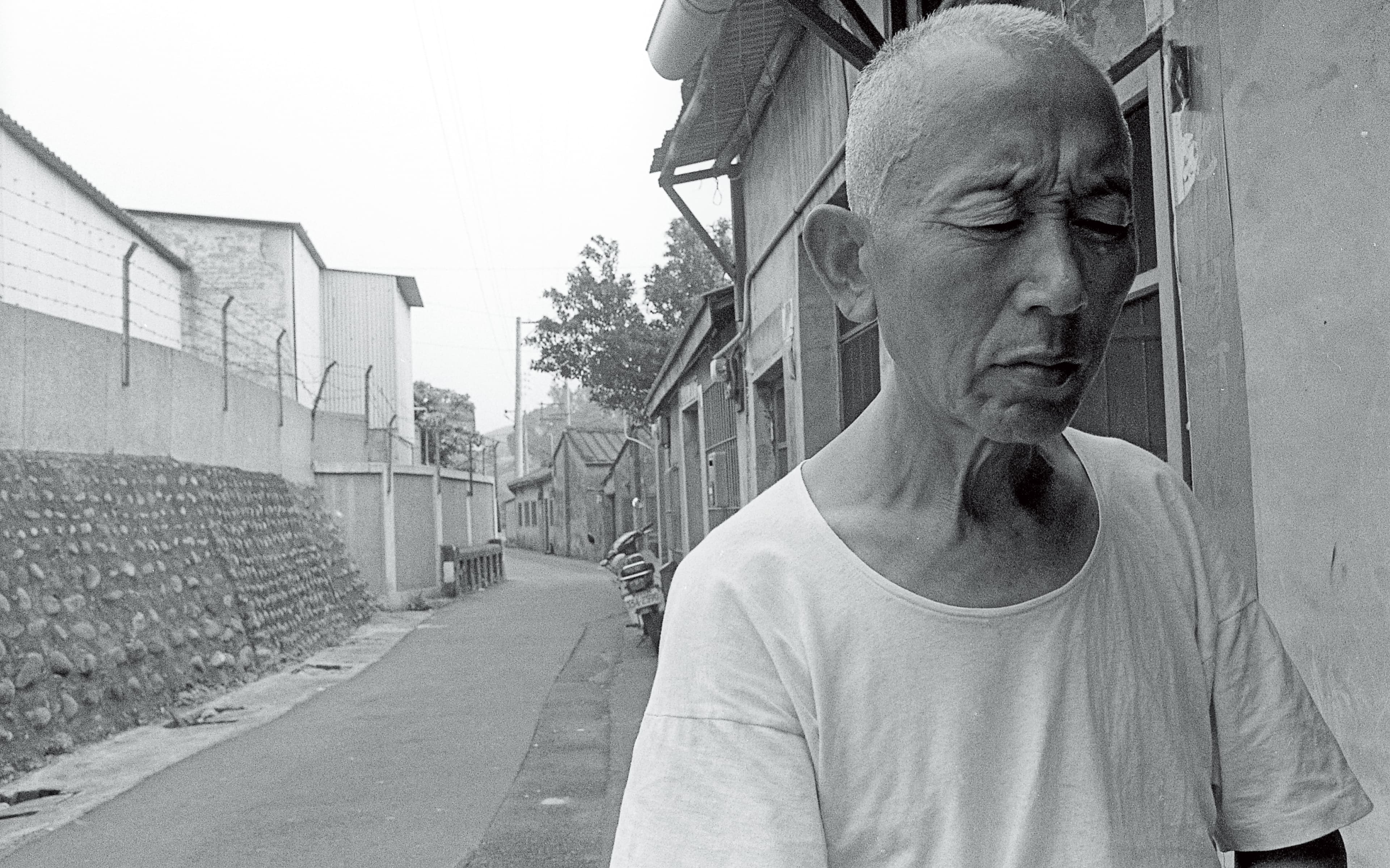 周子飛當年被救出後,媒體在張雄家門口拍攝張雄(圖)。時移勢易,周子飛如今對照片左方那面石牆仍有印象。(蔡明德攝)