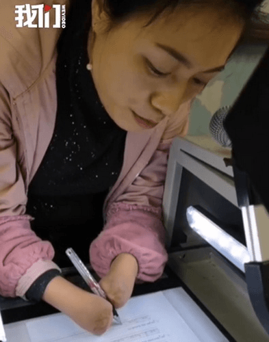 杜宣梅平時寫字需要用雙臂夾著筆,若要打開投影機則用雙臂夾著長棍開啟開關。(翻攝自新京報我們視頻)