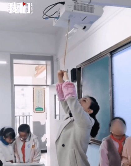 杜宣梅平時寫字需要用雙臂夾著筆,若要打開投影機則用雙臂夾著長棍開啟開關。(翻攝自新京報我們視頻)