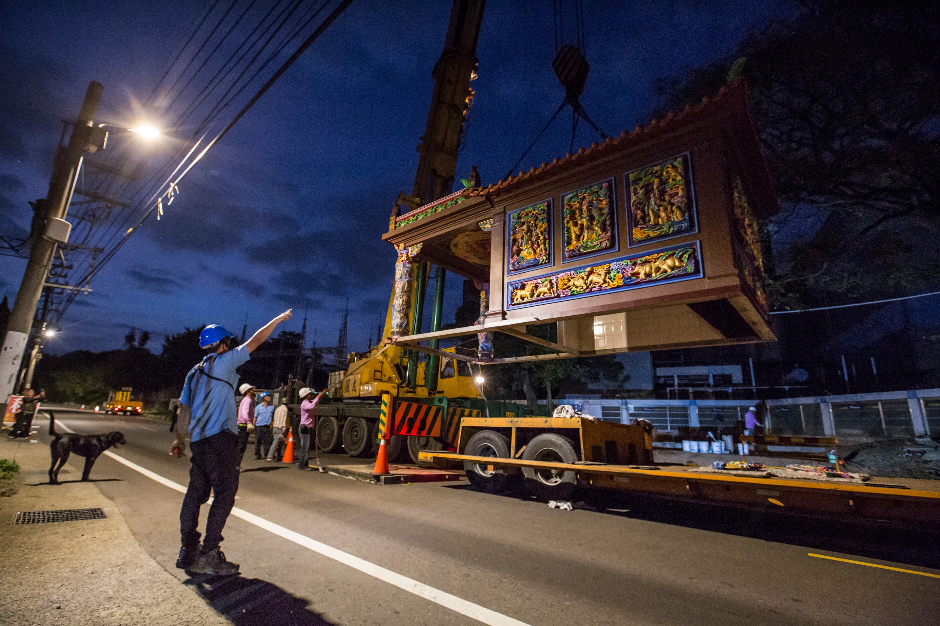 工程人員將吊車掛勾掛上廟宇屋頂，一座9坪大的土地公廟瞬間騰空而起，緩緩穿過2棵樹中間，不偏不倚地落在風水師指定的基座上。