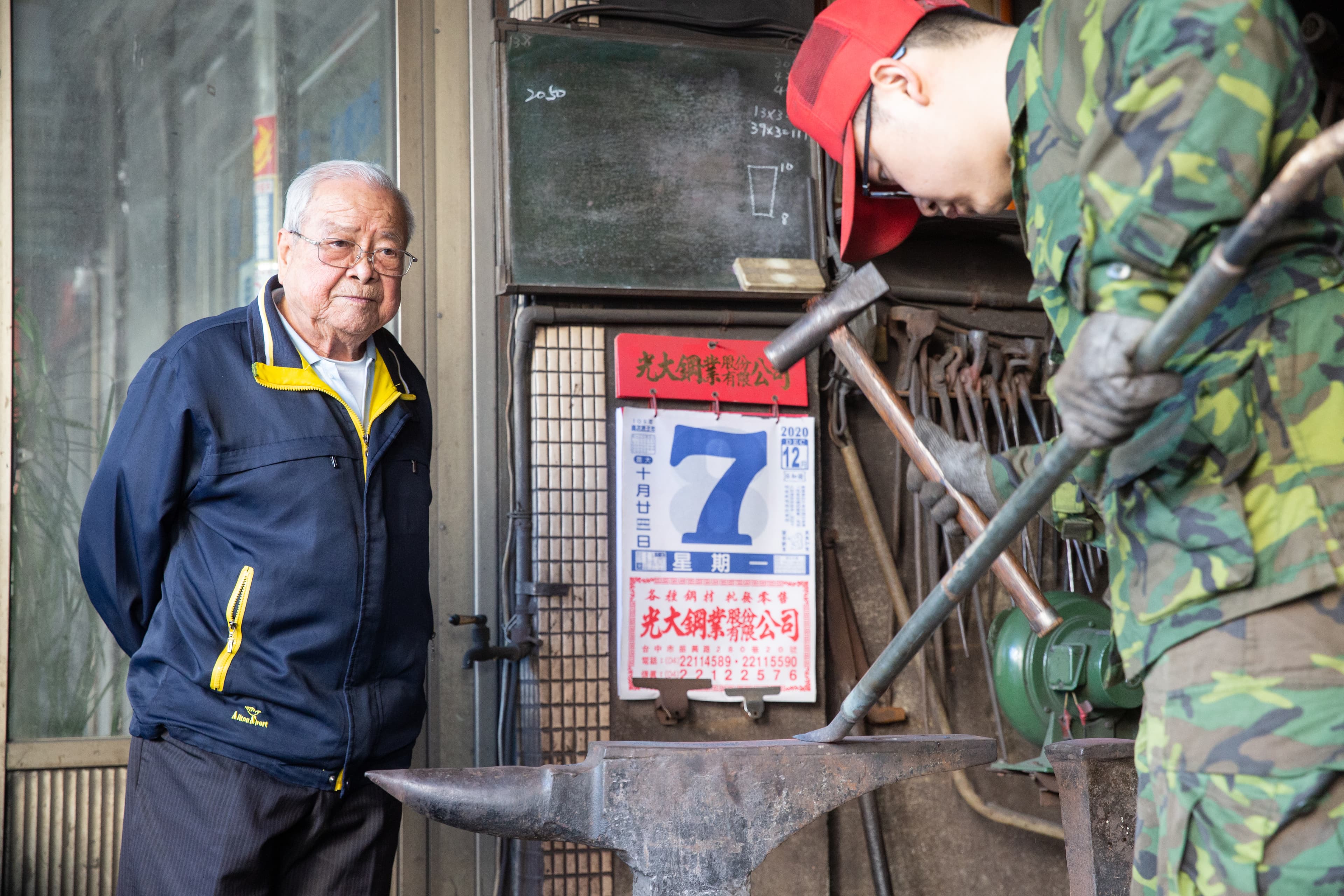 蔡進永的阿公、第一代蔡慶隆(左)雖已退休,仍常到店面看孫子(右)打鐵。