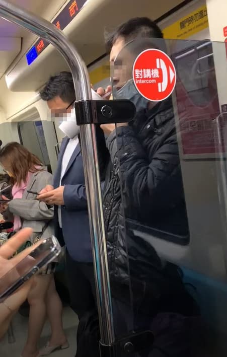 一名身穿黑色外套男子在捷運車廂內拉下口罩狂喝飲料。(讀者提供)