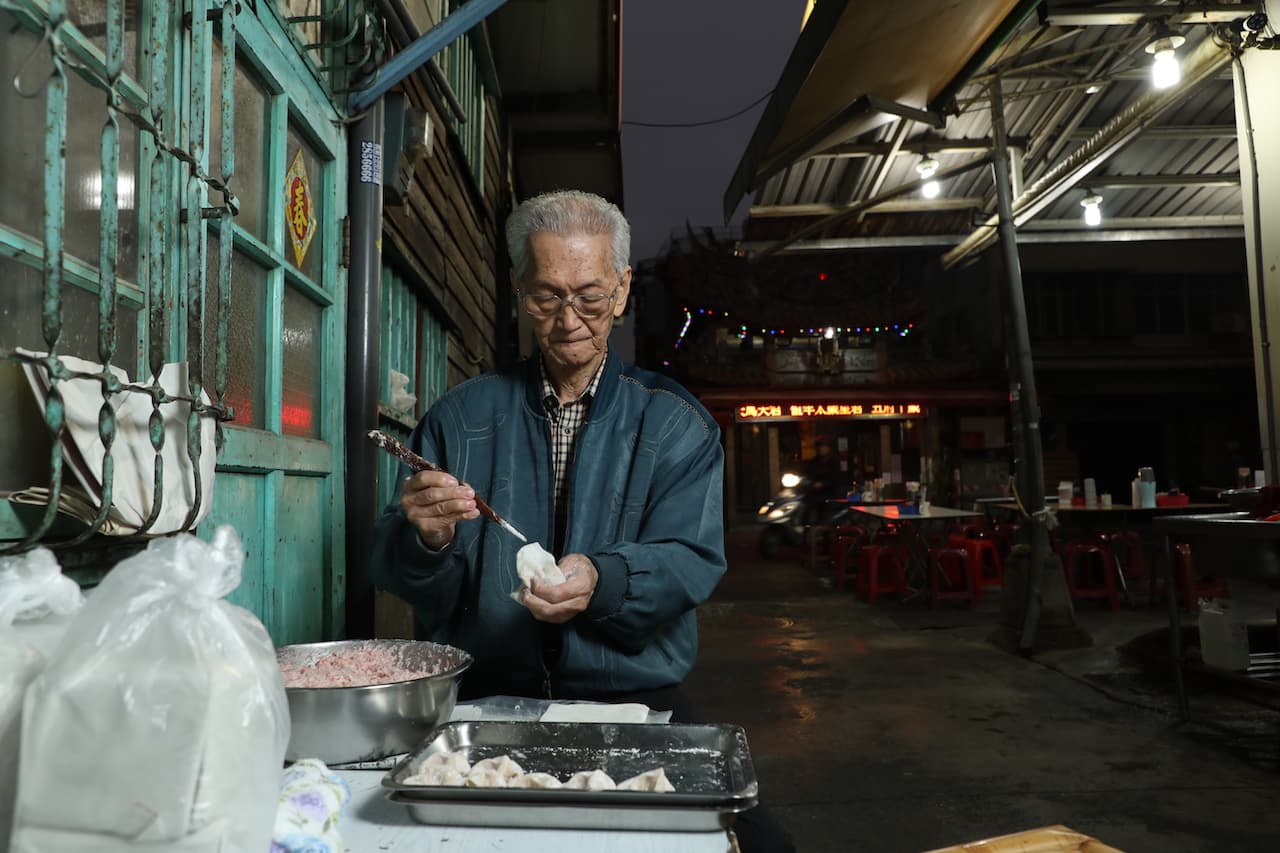 創始人許秉乾（黑乾）在矮房子旁靜靜地包著餛飩，彷彿時間緩下，日子靜好。