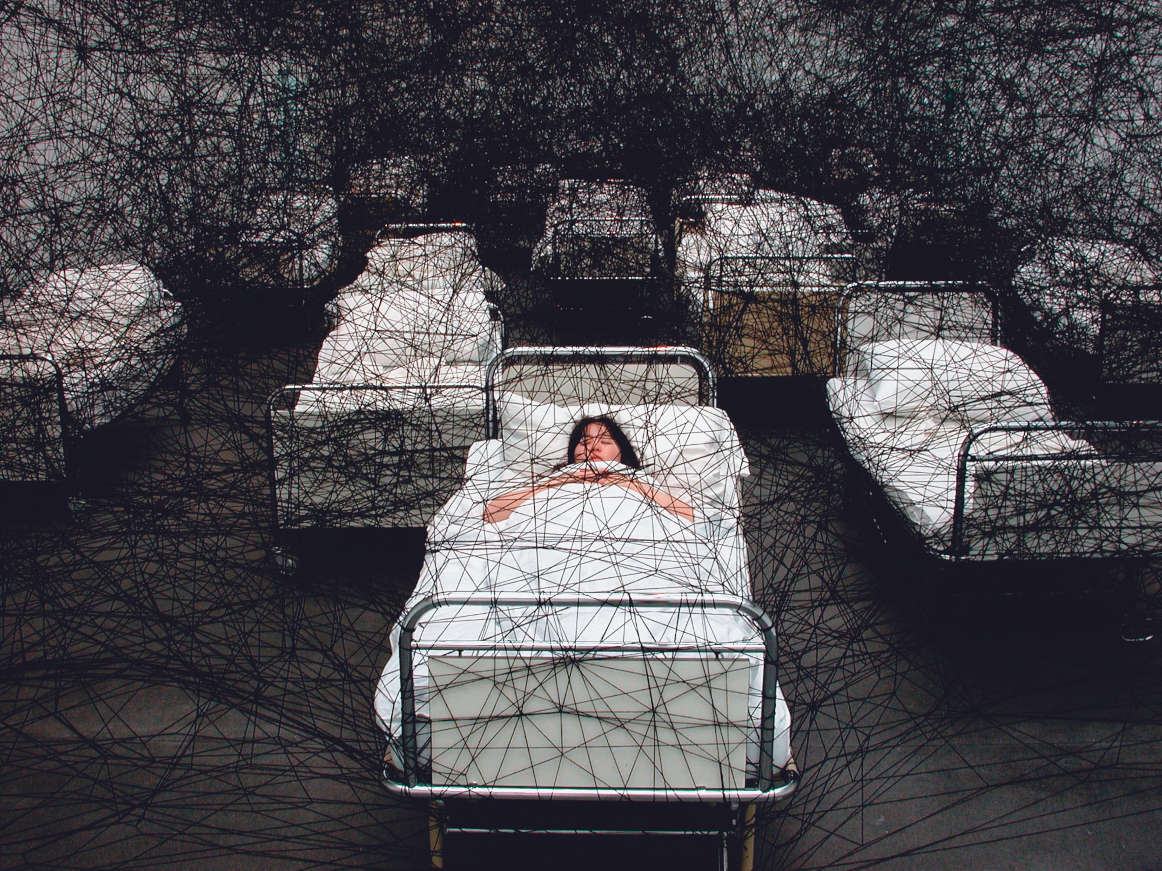 塩田千春結合裝置與行為的作品〈在沉睡中〉(During Sleep),她躺在床上睡覺,床則象徵了人生的起點與終點。(塩田千春提供)