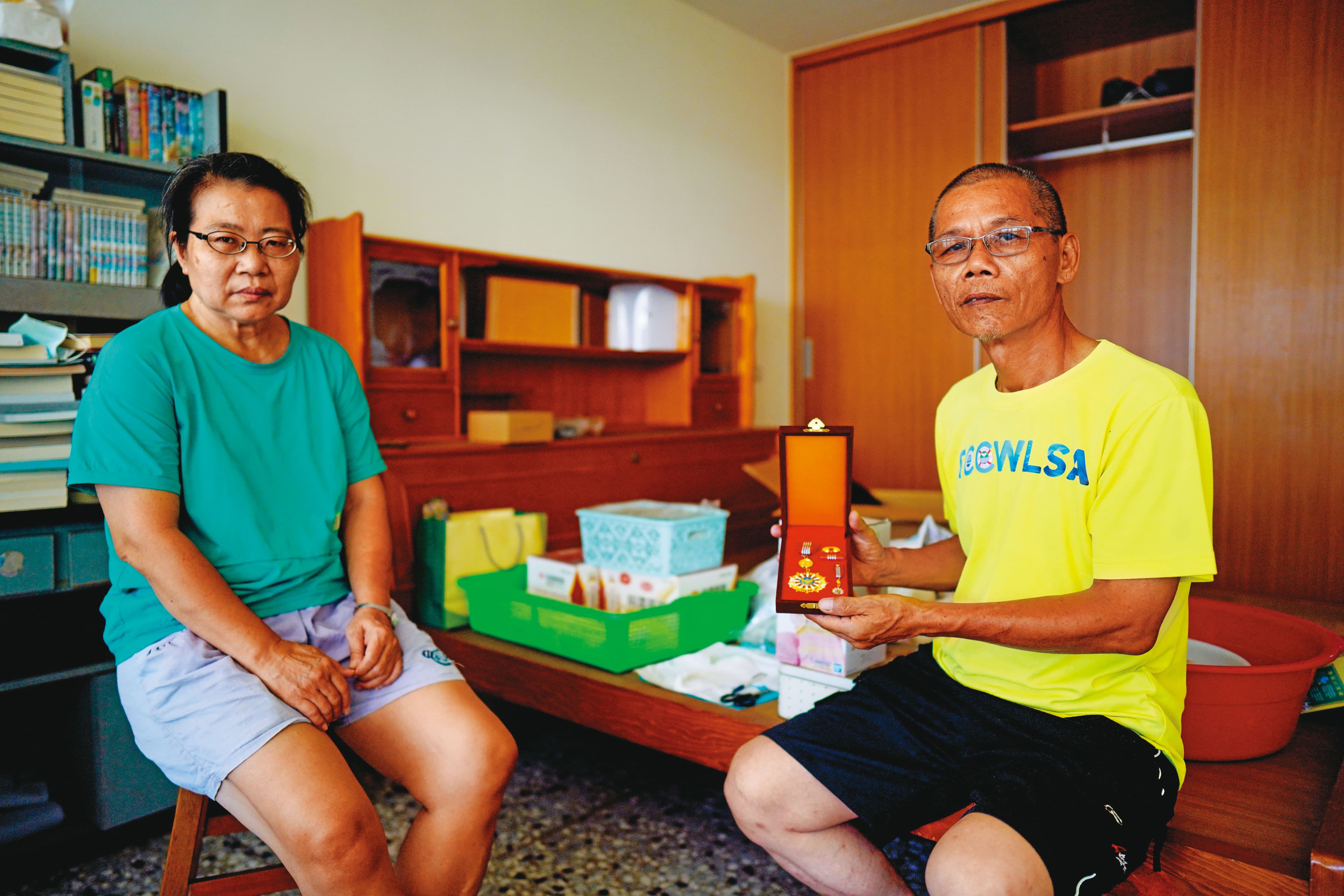 母親梁春子(左)、父親陳貴森(右)拿著勳章在陳志帆房間拍照,母親強忍悲傷,一度說不想拍了。(林韋言攝)