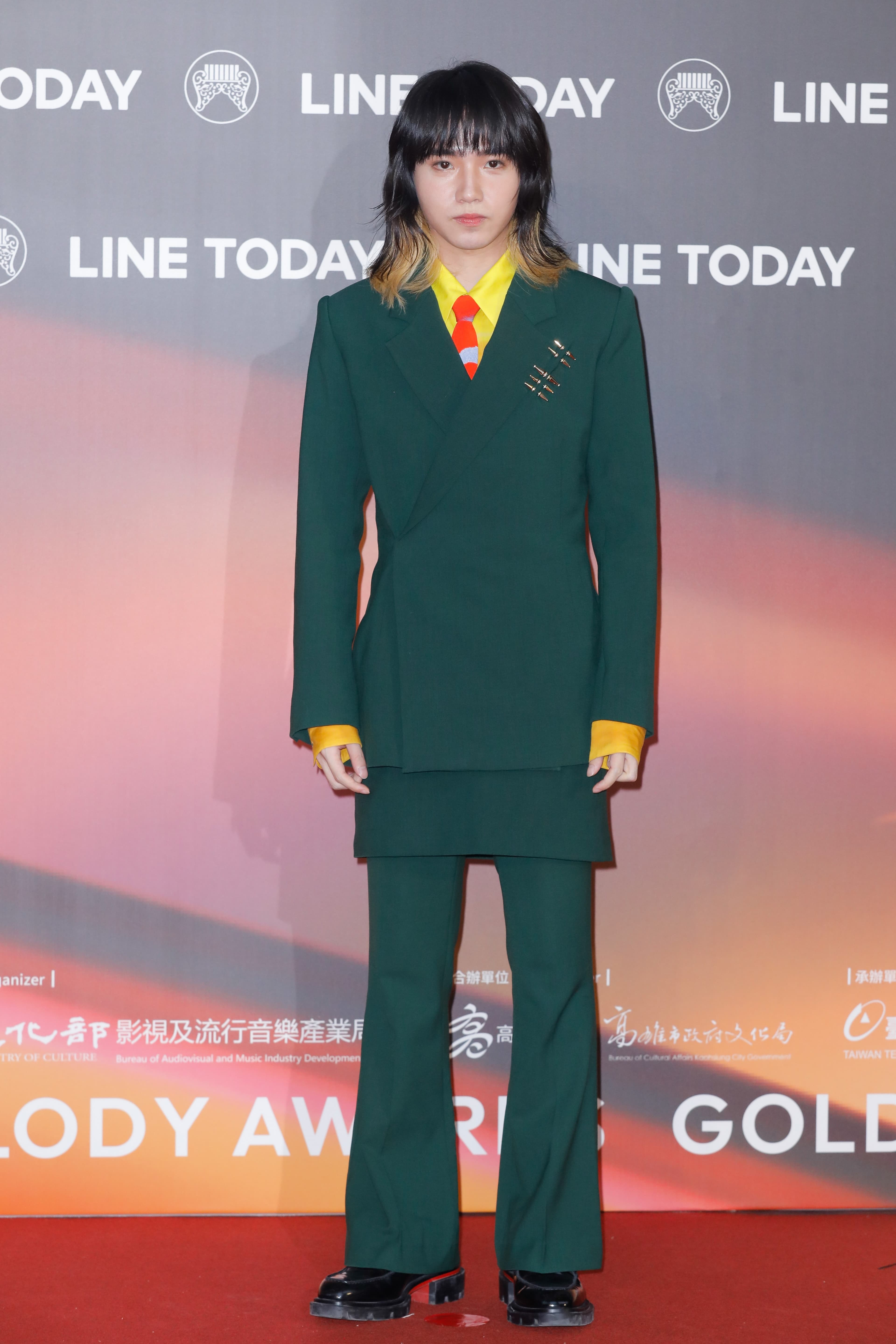 持修身穿全套綠色正裝,搭螢光黃色襯衫及亮橘色領帶紳士中洩露童趣感。