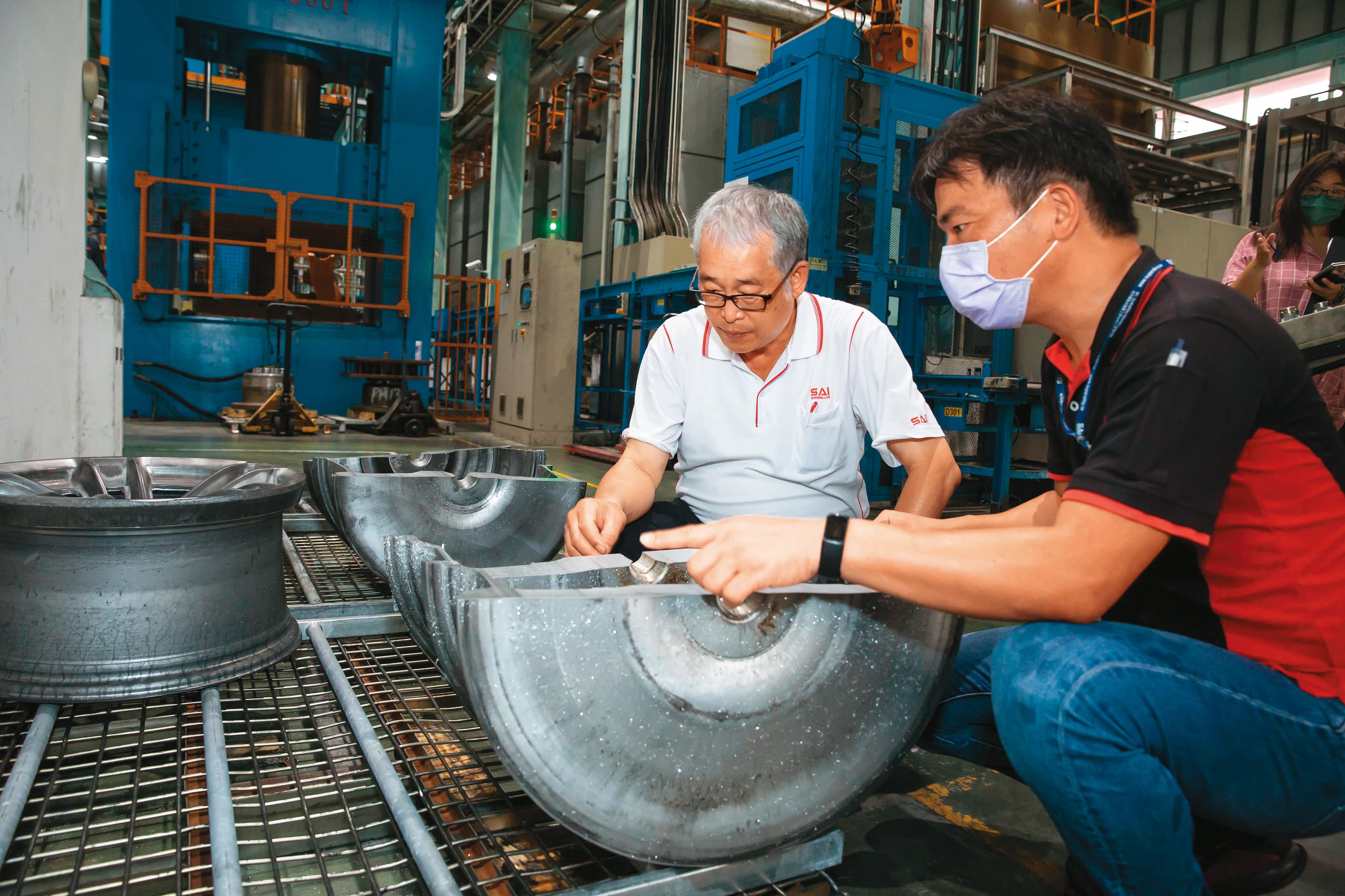 黃聰榮（左）重視製程基本功與細節，巡廠時與員工一起檢查經過粗鍛、細鍛的輪圈厚薄度是否符合設定範圍。