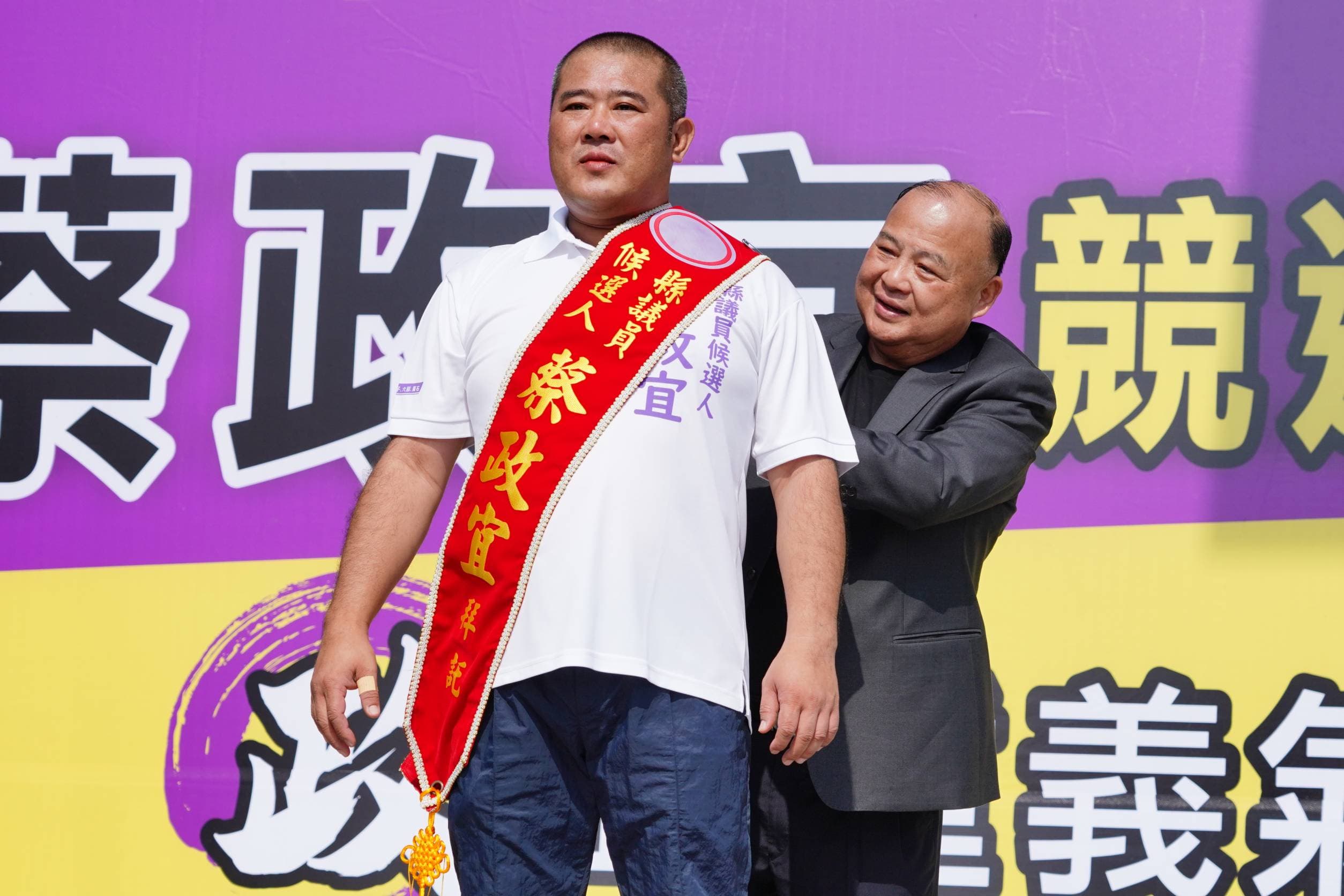蔡政宜的叔叔蔡慶源(右)替他掛上布條。