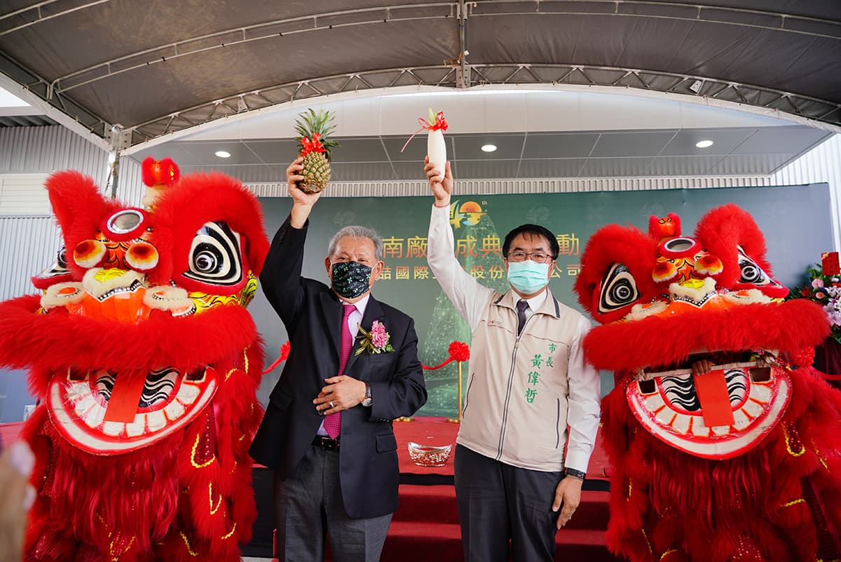 美喆台南新廠落成,董事長陳本源(左)與台南市長黃偉哲高舉鳳梨與菜頭(白蘿蔔)要取得好彩頭。