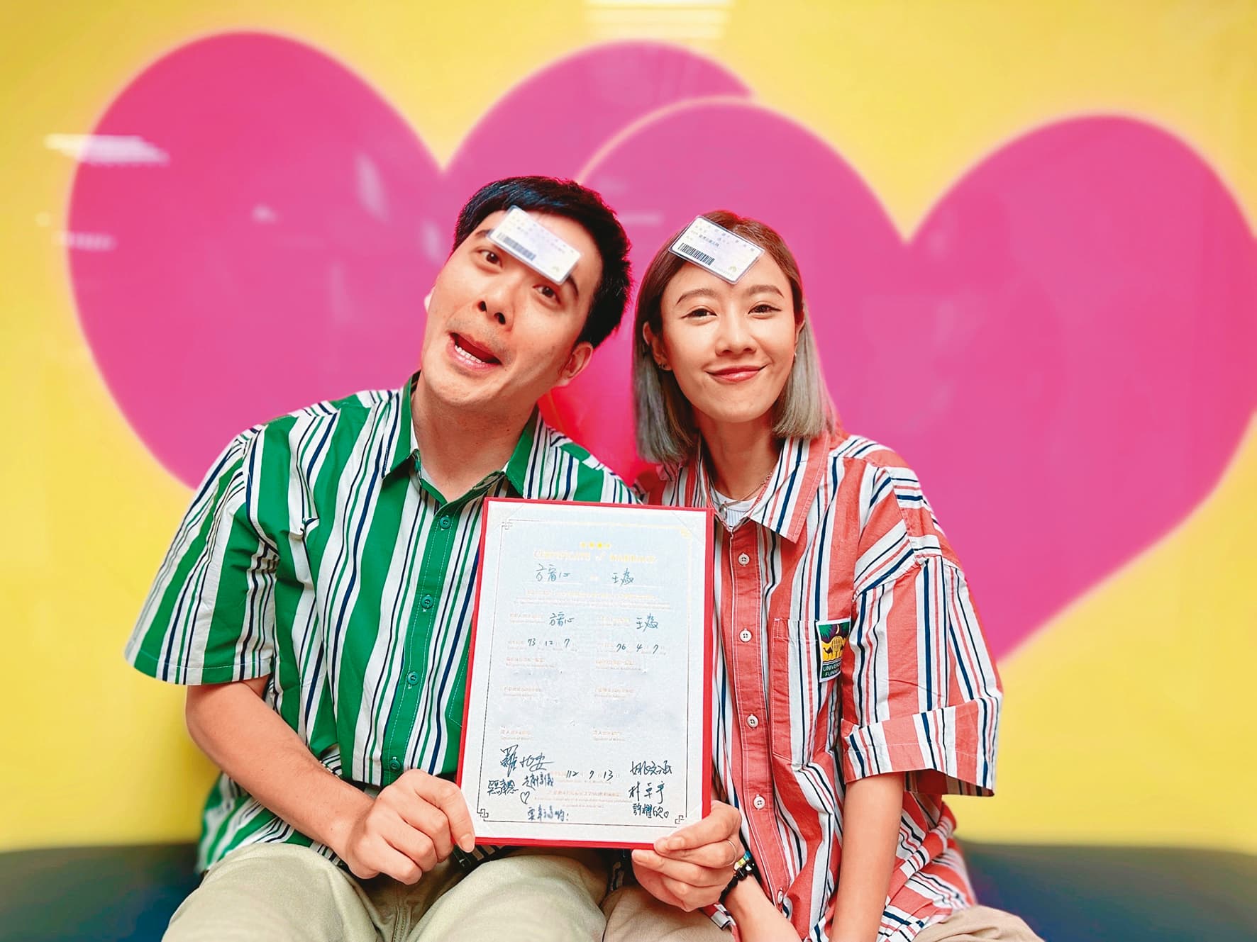 王為(左)和方宥心(右)穿著情侶襯衫,額頭貼著身分證、手拿結婚證書開心合影。(王為提供)