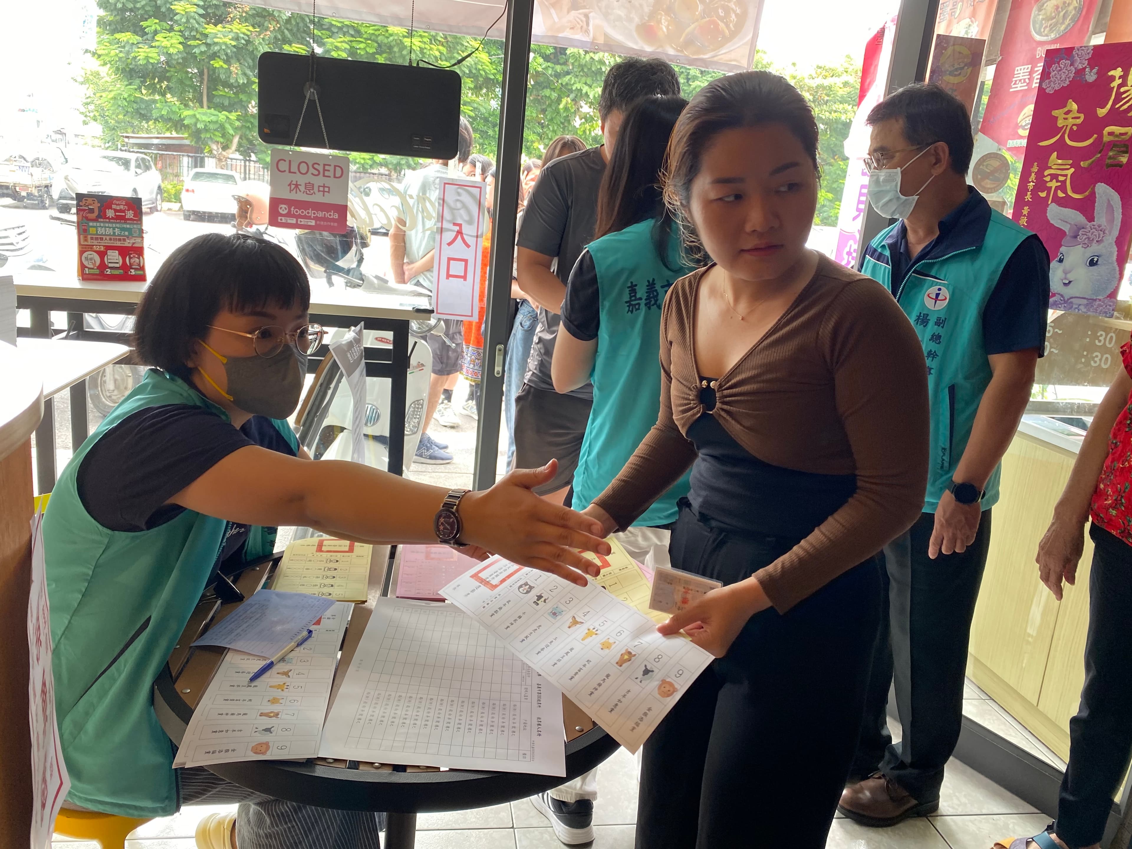 越南新住民紅青(右1)領取模擬選票後,在嘉義市選舉委員會人員引導下,前往圈票處模擬圈選心目中的候選人。(移民署嘉義市服務站提供)