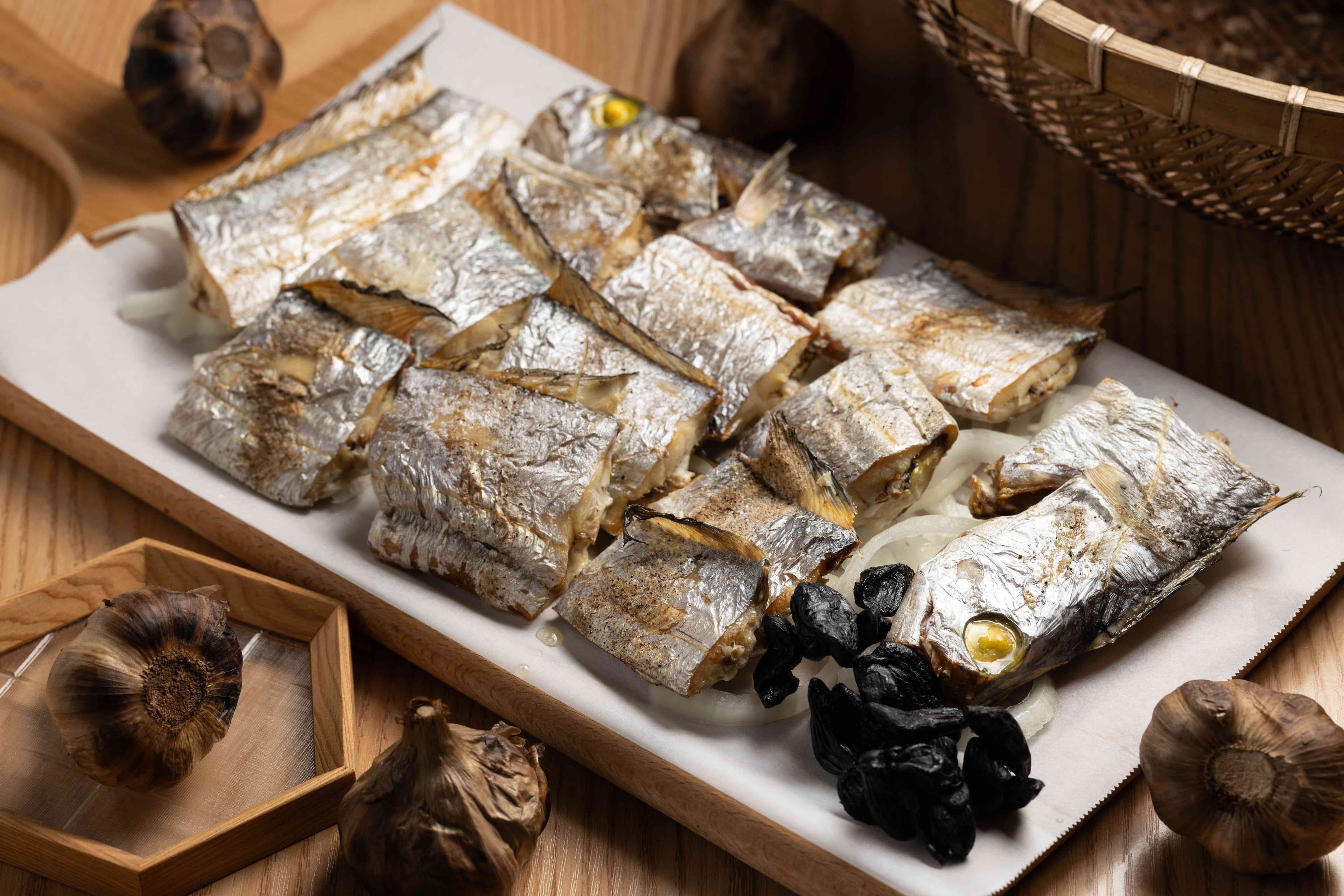「鹽烤油帶魚」使用大武沿海特有魚種,油脂豐厚,搭配黑蒜頭一起吃更美味。(750元/條,依時價為準)