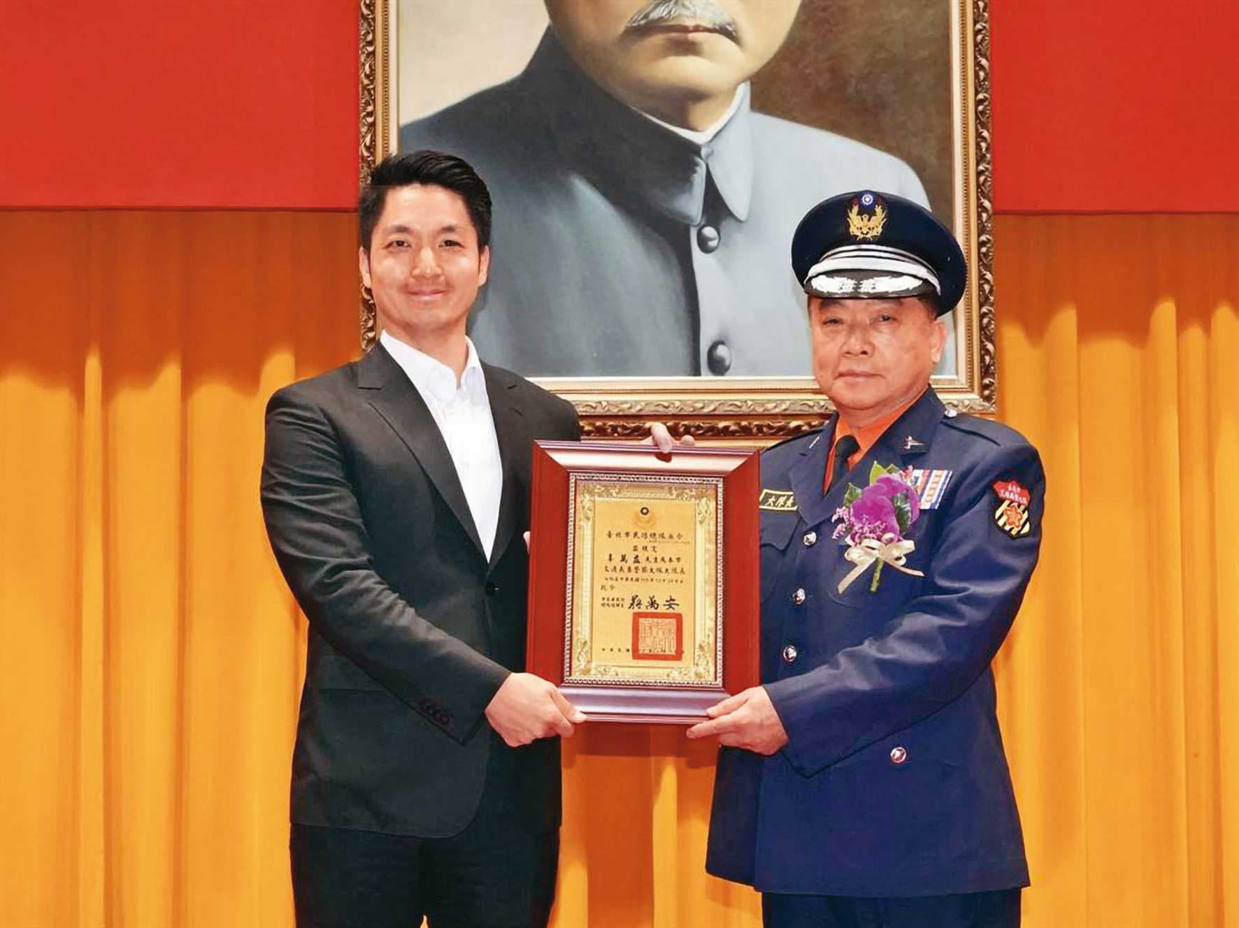 辜萬益(右)升義交大隊長時,曾被檢舉超齡,最後仍從台北市長蔣萬安(左)手中接下聘書,順利就任。(翻攝畫面)