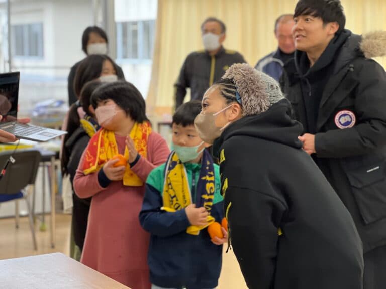 米希亞(右前)送上巡演的毛巾給災民,也熱情合影。(翻攝自米希亞官網)