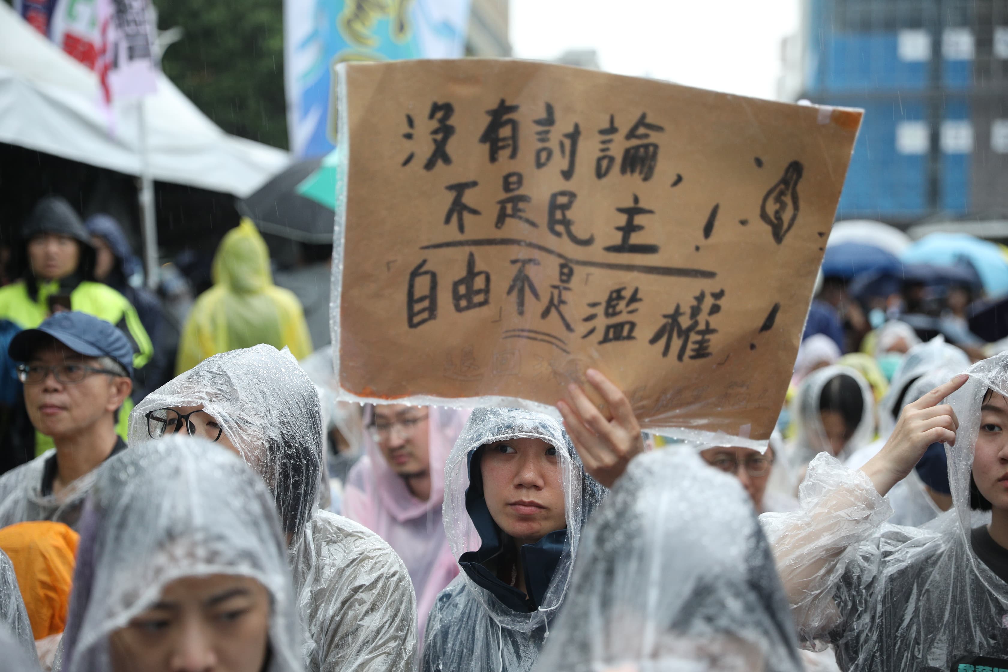 民眾穿著雨衣聚集在立法院外,高舉「沒有討論、不是民主」的口號,抗議藍白強推法案。