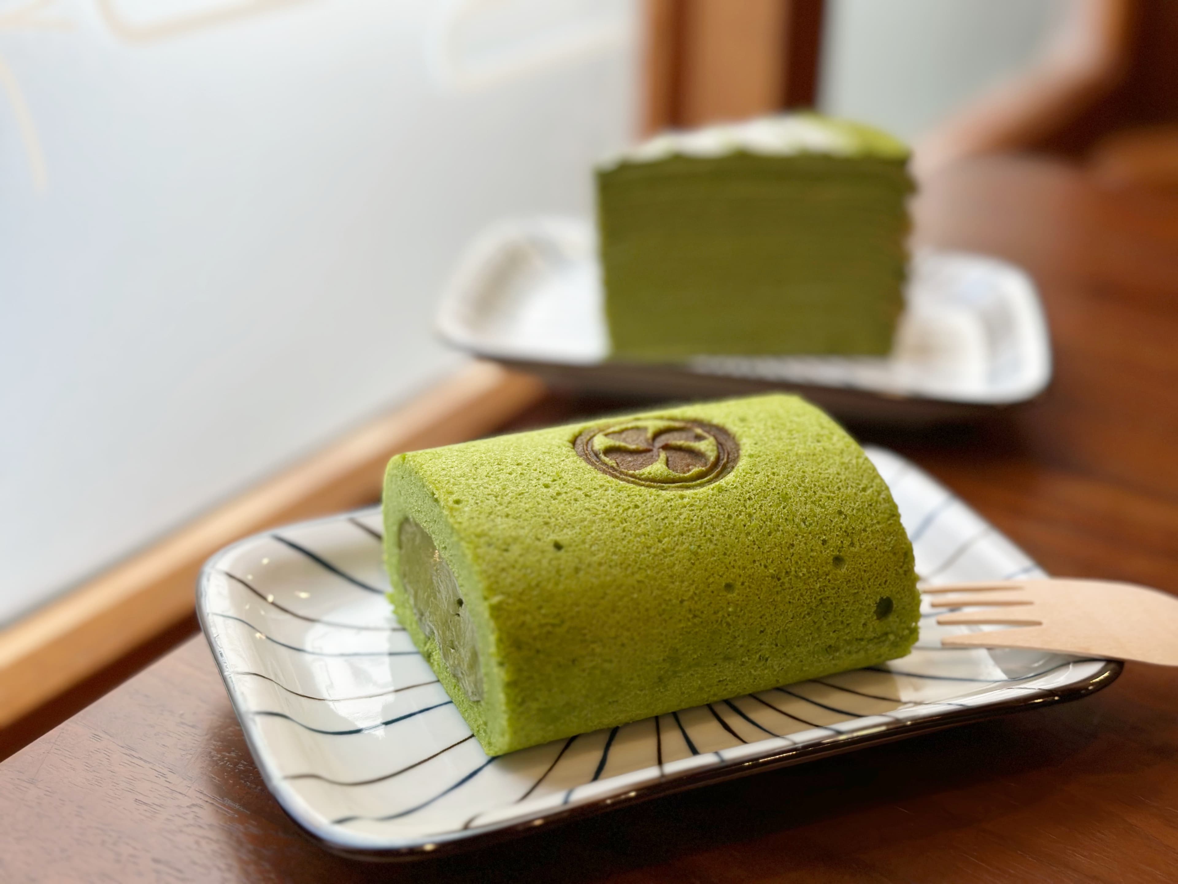 手作「宇治抹茶千層」(後,180元/份)與香濃的「宇治抹茶生乳捲」(前,90元/份)。
