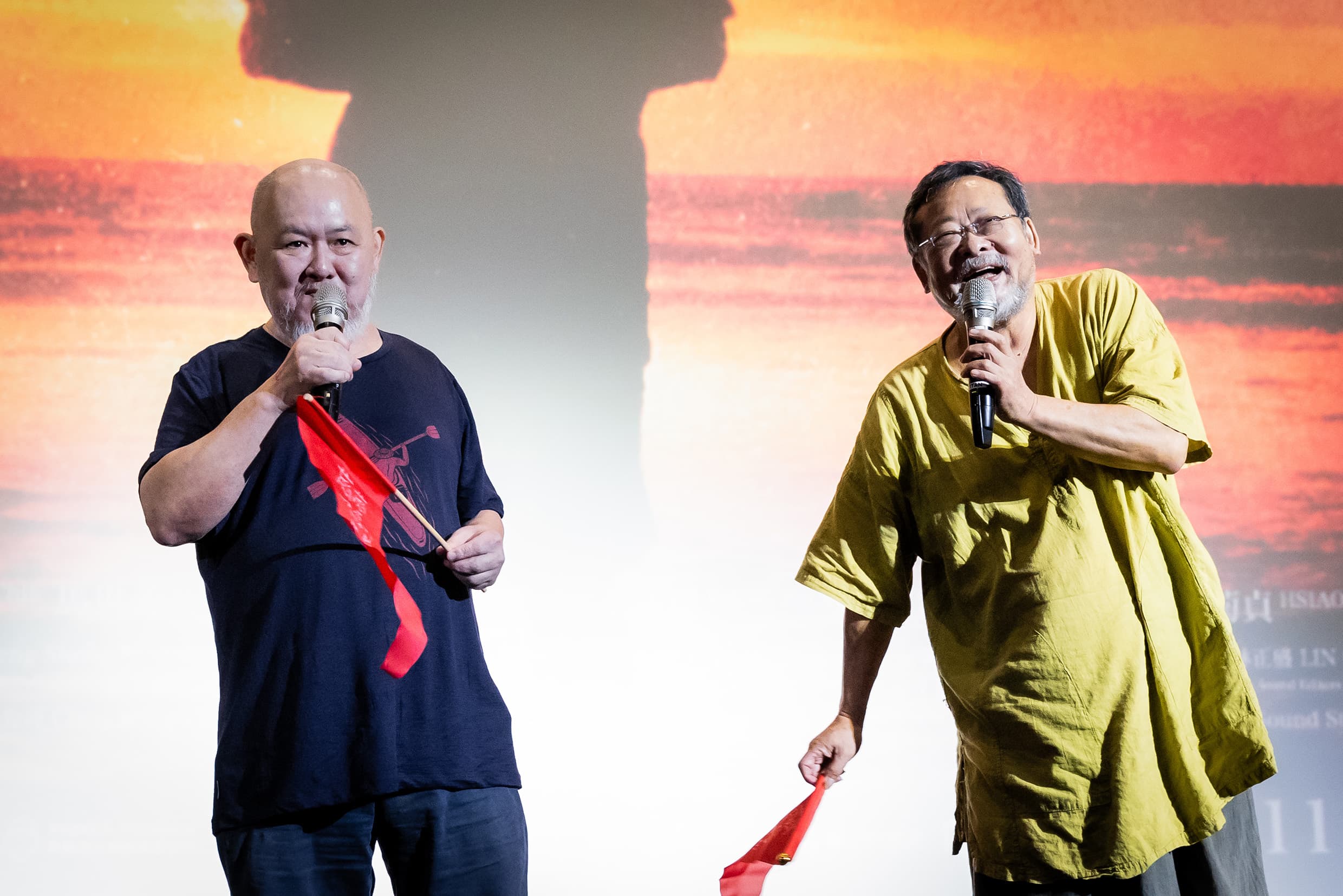 《撼山河 撼向世界》陳明章(右)與導演林正盛(左)在映後帶領觀眾一齊揮舞手中的紅旗。(我們之間影像製作有限公司提供)