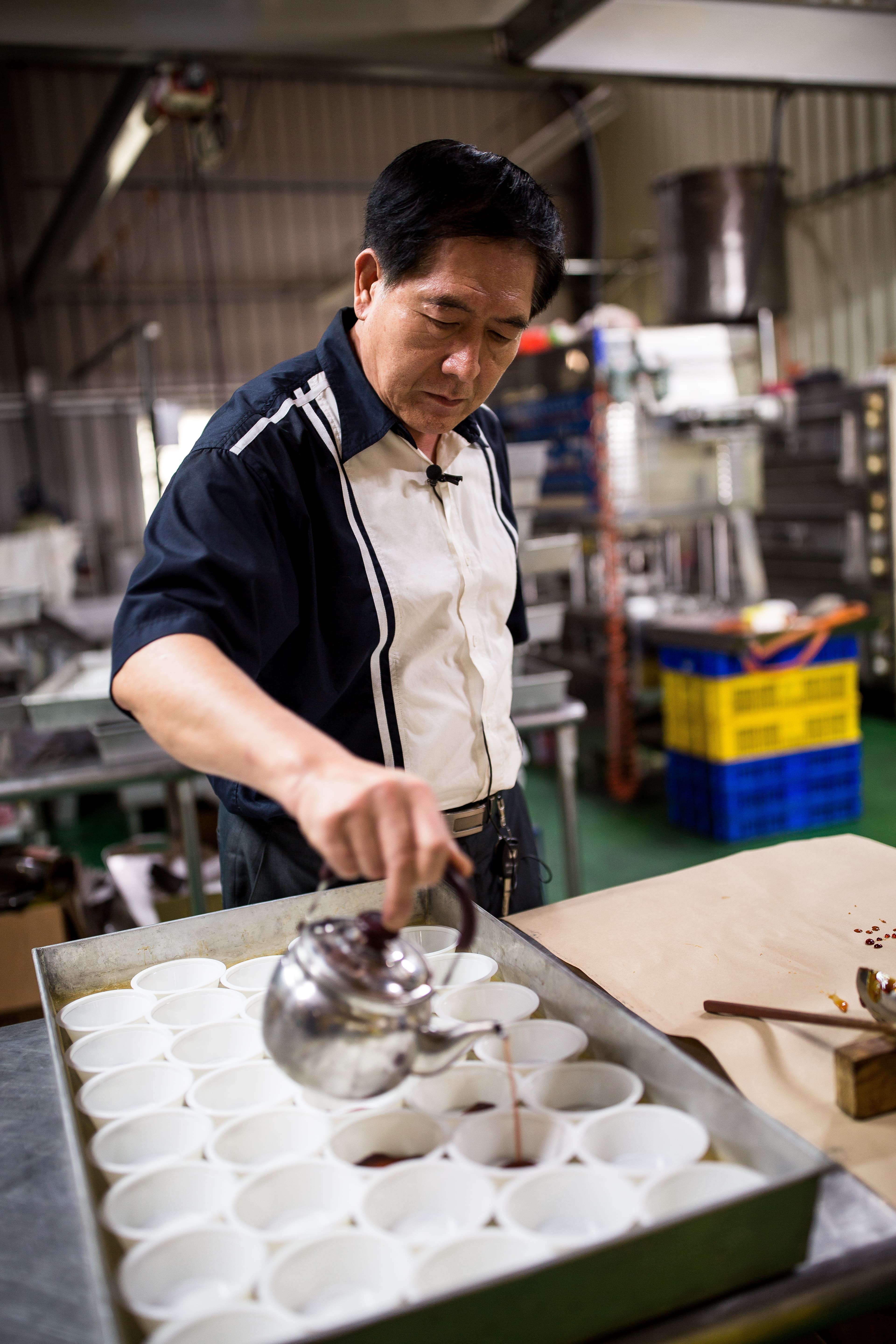 吳文耀拿著自製的銀色茶壺,準確地在布丁盒內內倒焦糖,長年下來,毋須使用磅秤,就能準確拿捏焦糖的份量。