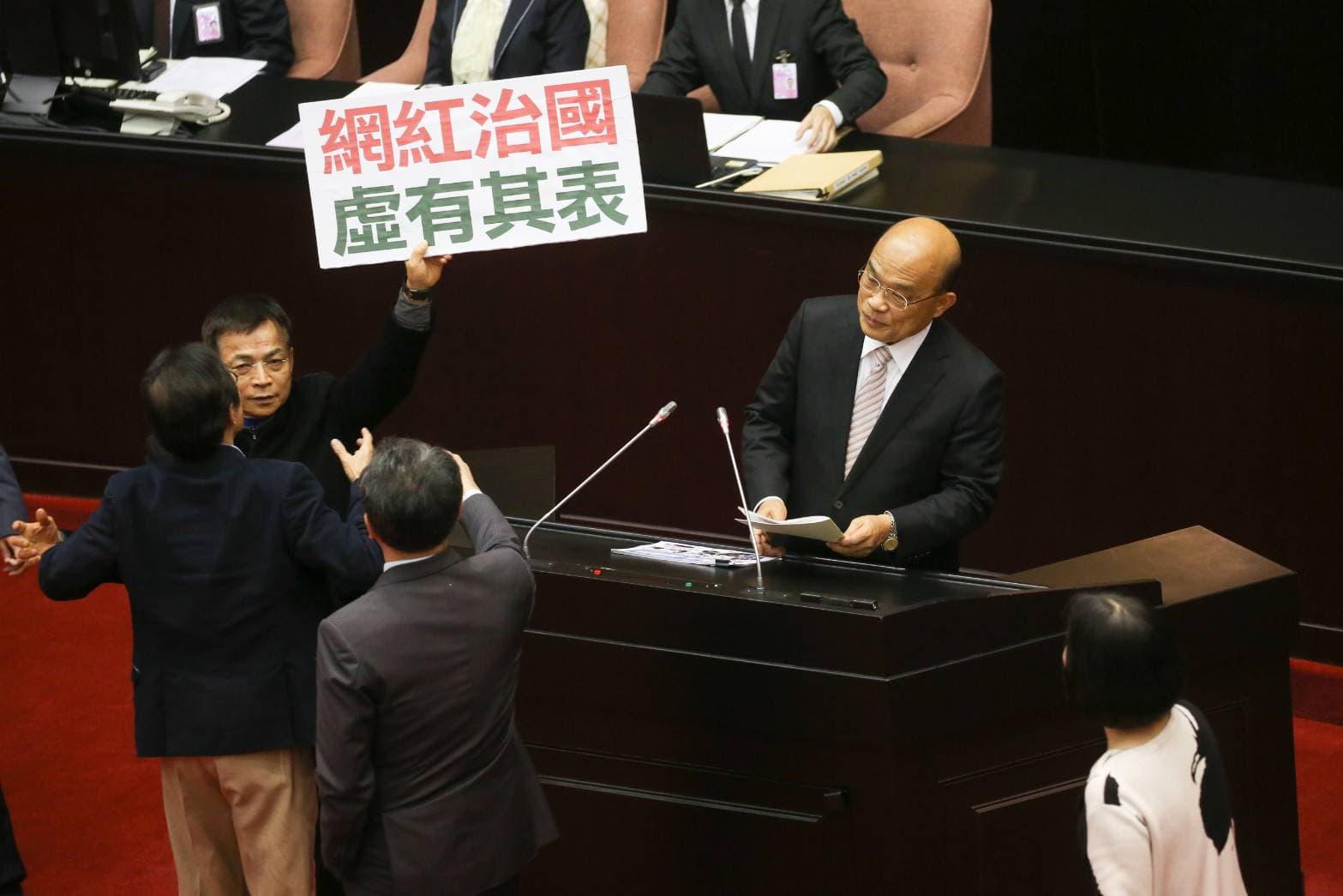 蘇貞昌上台報告時,國民黨立委賴士葆還是在他身旁舉著標語抗議。