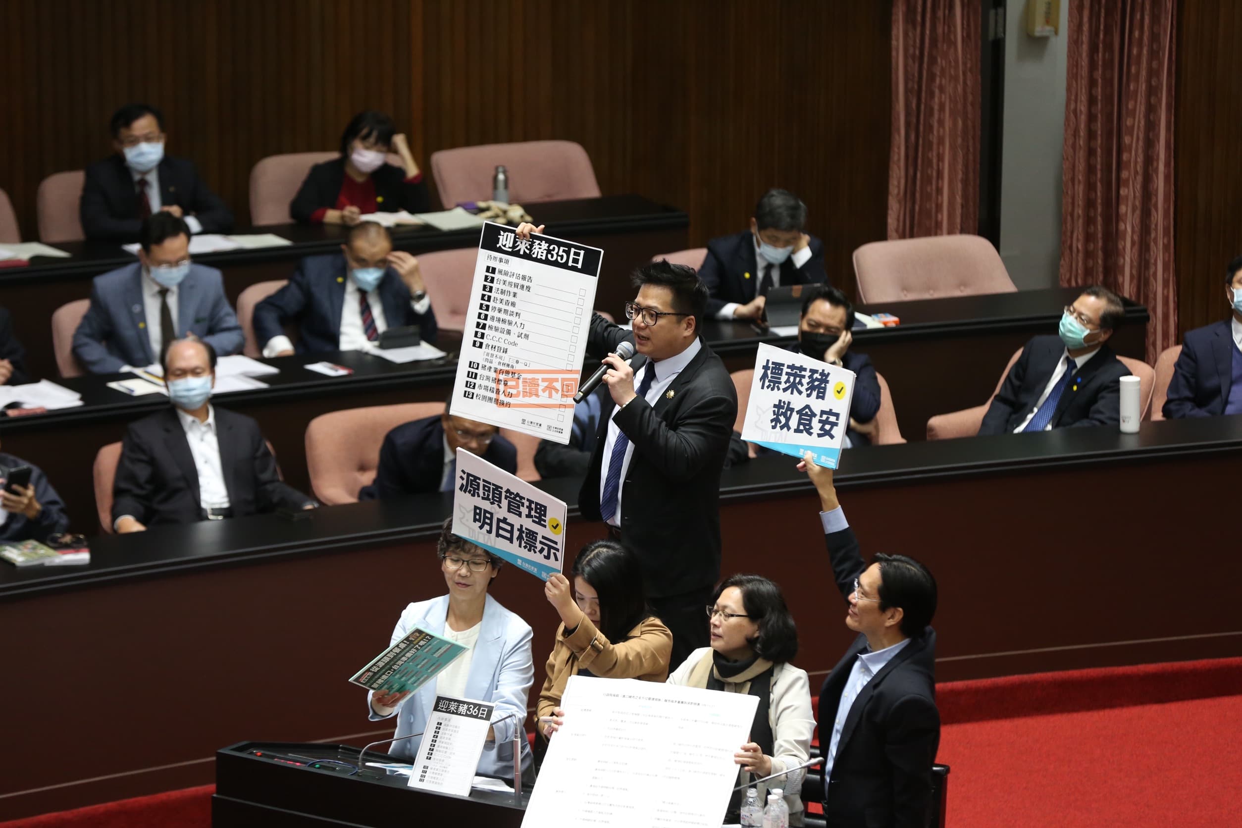民眾黨立委邱臣遠(舉「迎萊豬35日」板者)質詢時,同黨立委在旁協助。