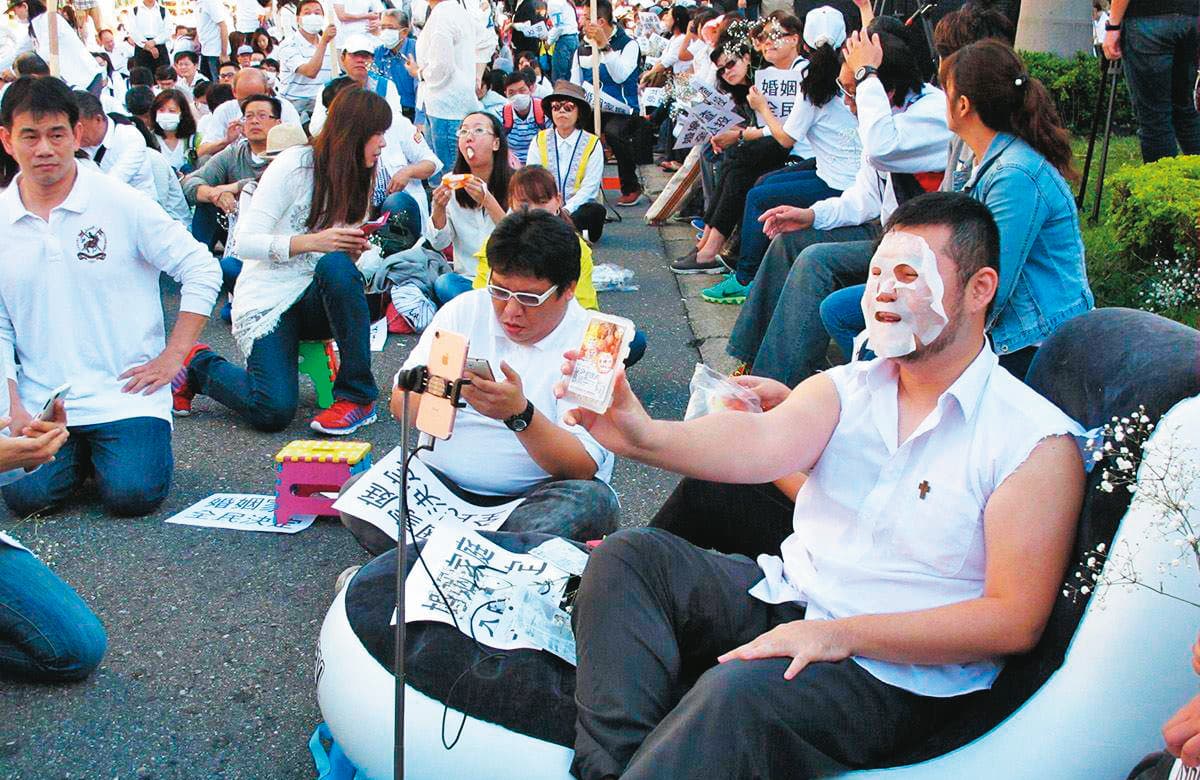在反對同性婚姻的宗教團體集會上,四叉貓(前右)會自創各種怪招吸引媒體目光,瓜分輿論效應。圖為他躺在充氣床上直播敷面膜。(翻攝自四叉貓臉書/PNN)