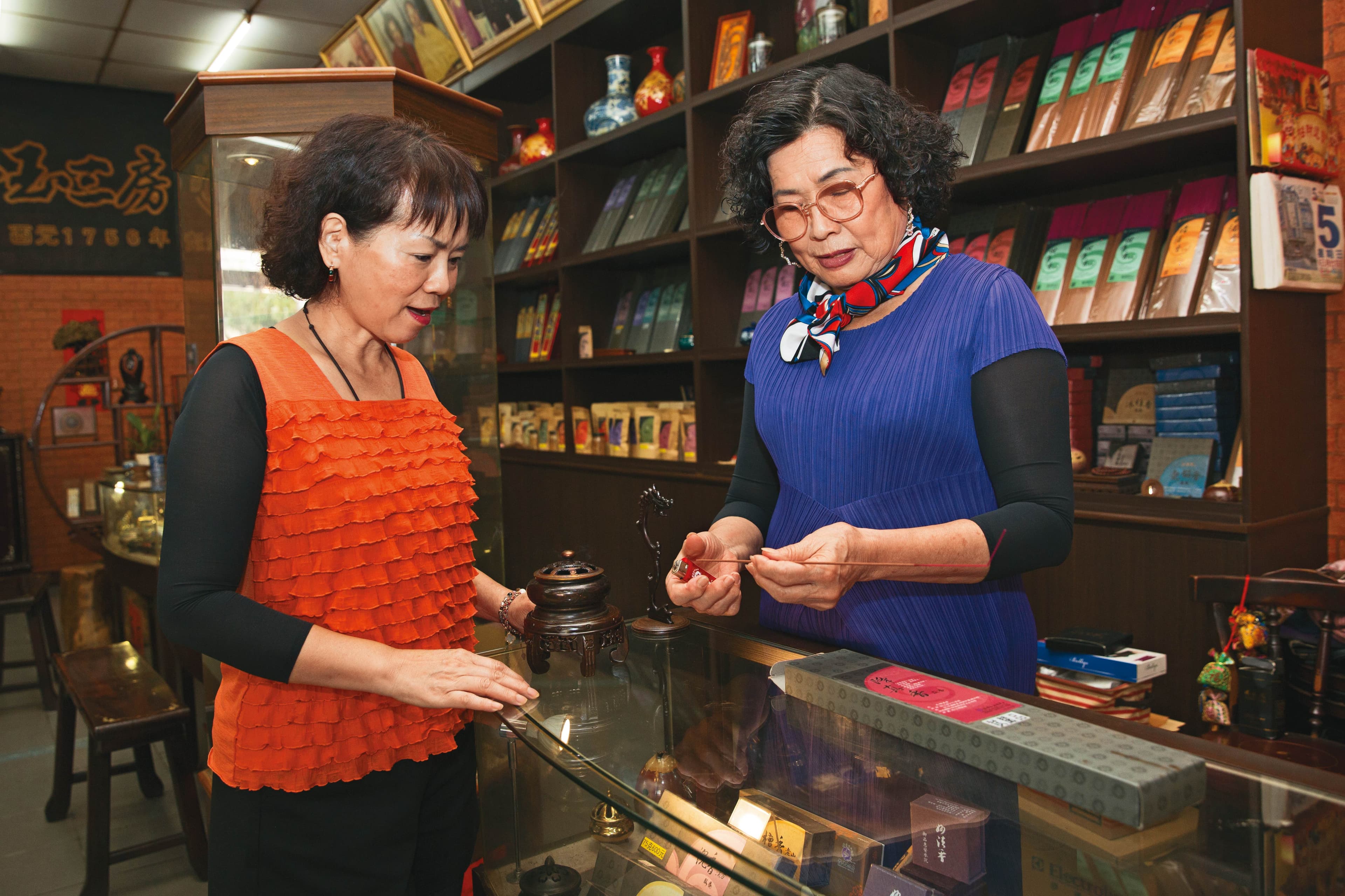 只要客人進店,第7代老闆娘洪寶真(右)一定點香讓客人試聞,詳細解釋何謂中藥養生香。左為顧客林小姐
