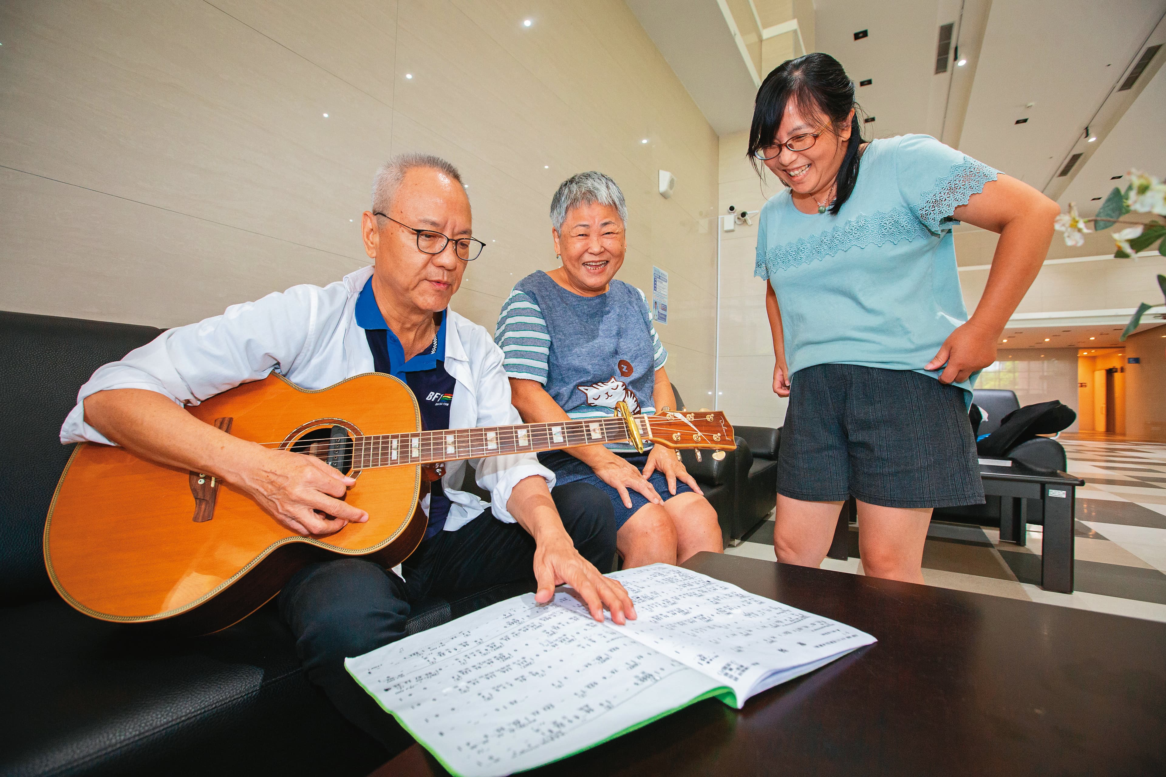 江希陸(左1)退休住進新北市府「青銀共居」社會宅,在大廳自彈自唱,與鄰居同樂。