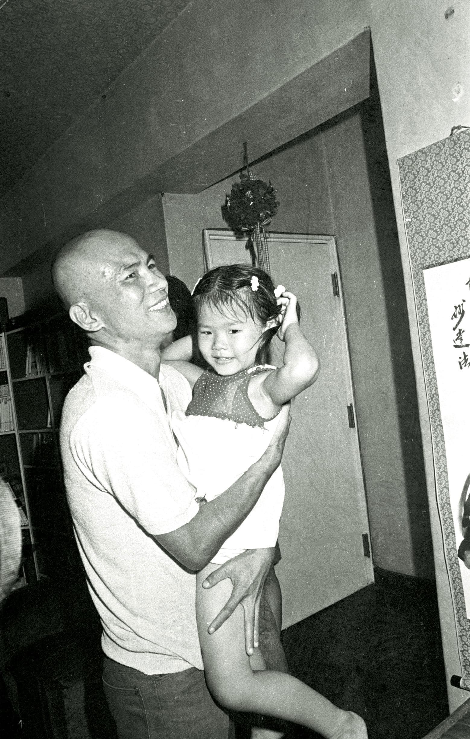 1984年,林義雄假釋返家,彼時因監所環境太差、天氣太熱,他理了個大光頭。圖為他返家後高興抱起外甥女。(中央社)